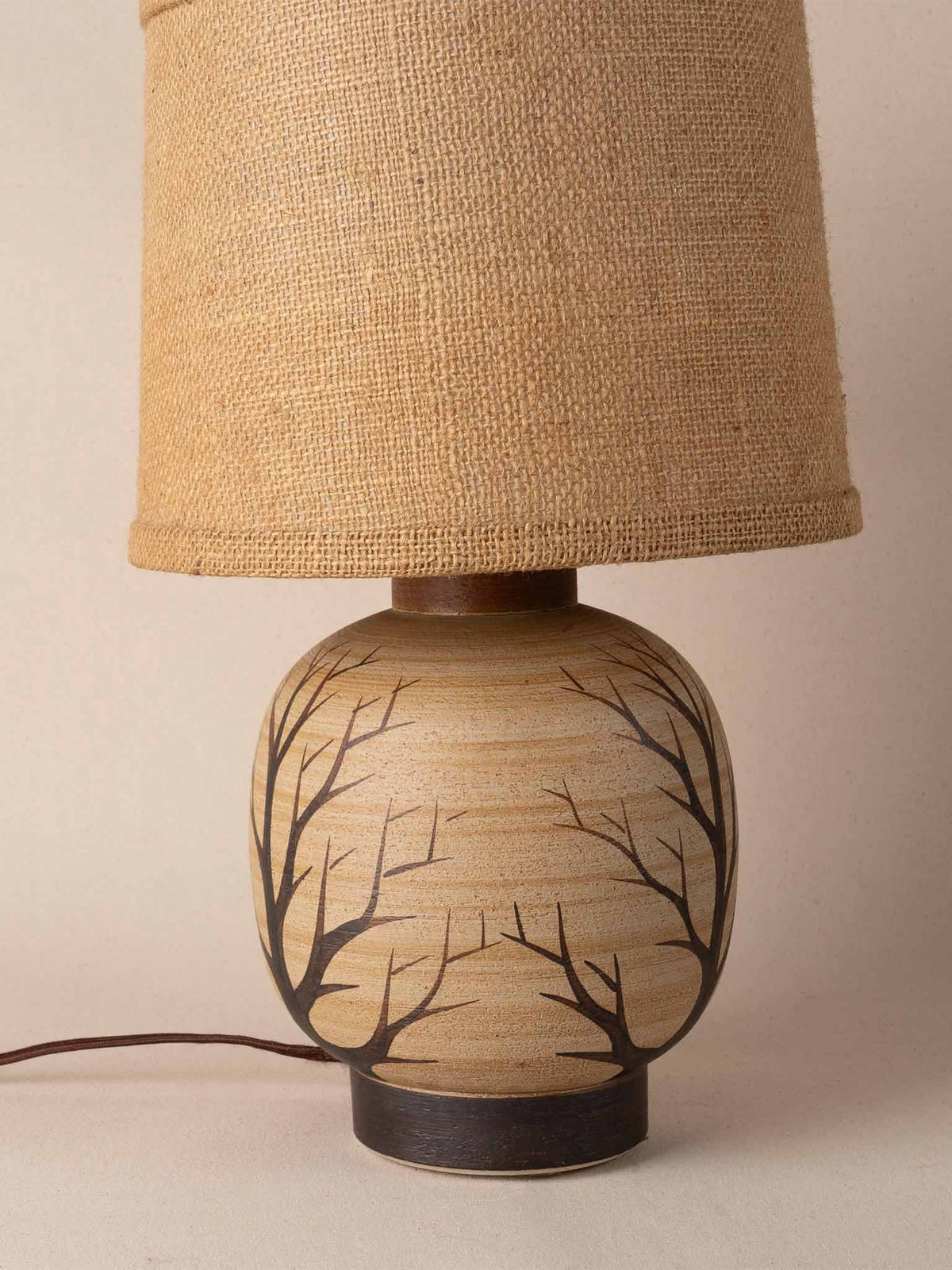 Small mid-century cream ceramic table lamp painted with black tree branches, on a dark plinth with a burlap drum shade
