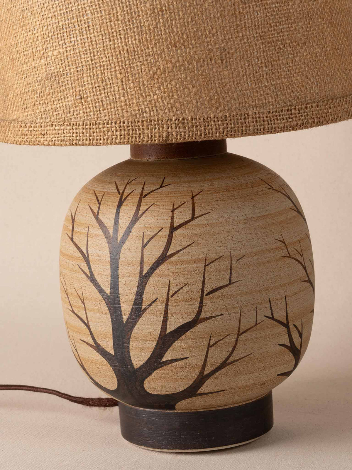 Small mid-century cream ceramic table lamp painted with black tree branches, on a dark plinth with a burlap drum shade