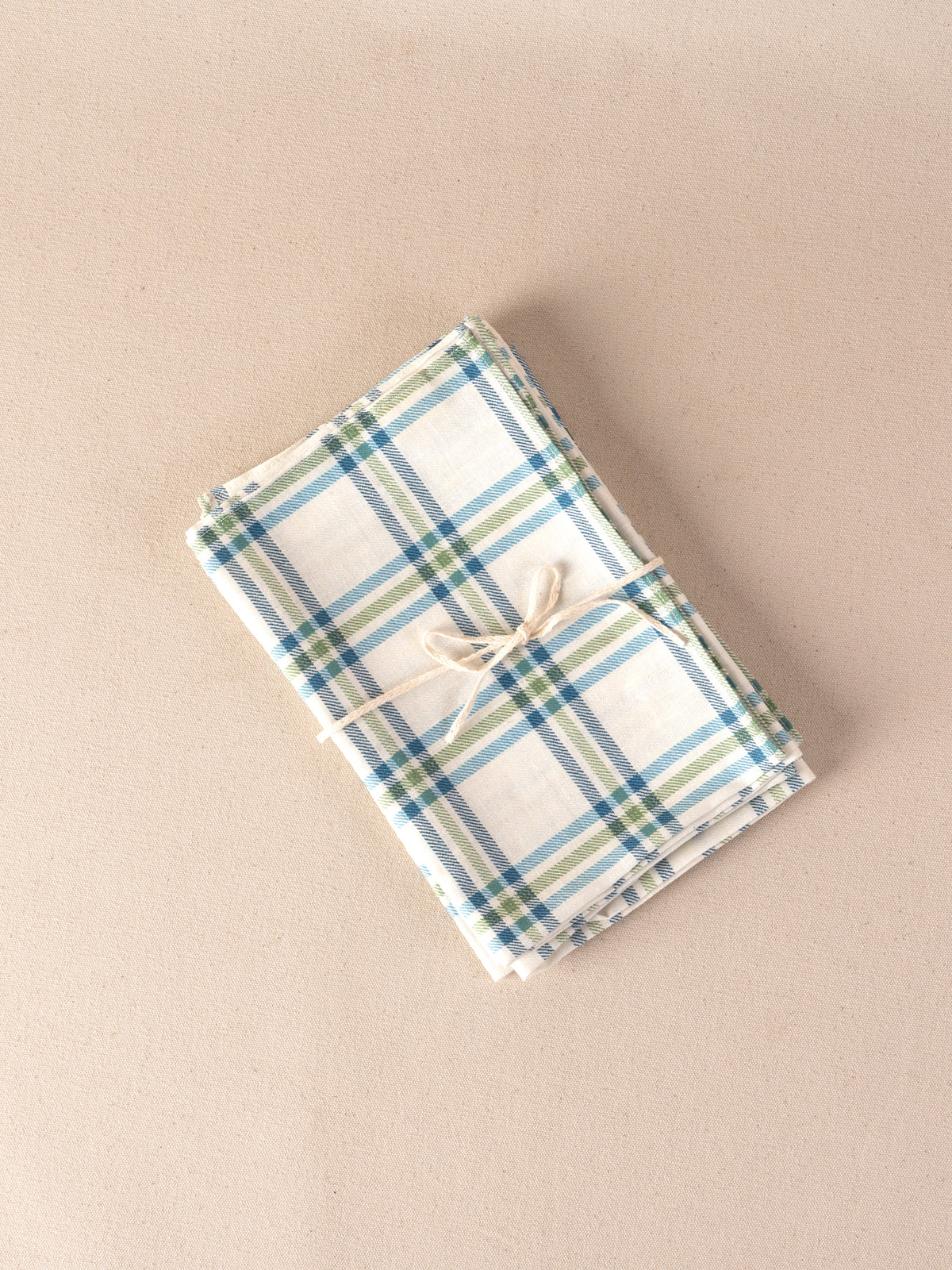 Four folded linen napkins in the Roger Plaid print in blue green